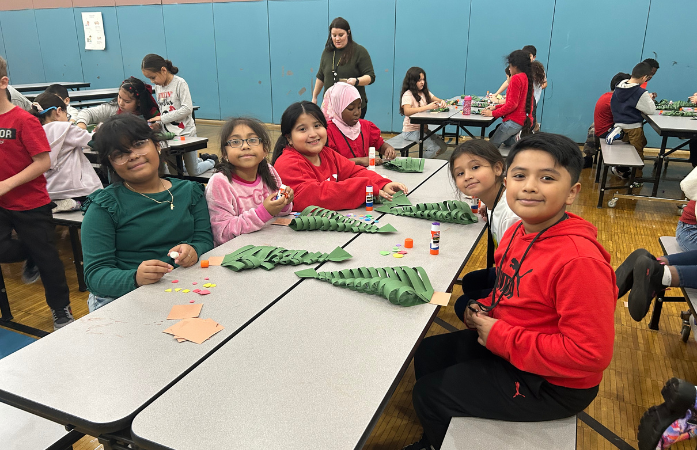 students sitting and smiling while working to decorate their paper Christmas trees